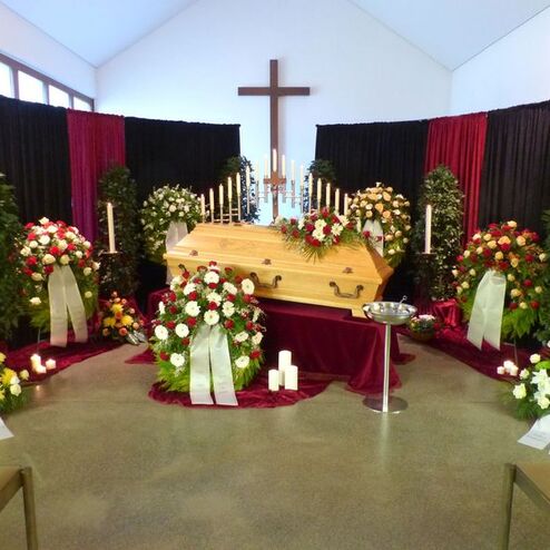 Blumenarrangements und Kerzen umgeben einen hölzernen Sarg in einer stilvoll dekorierten Trauerhalle.