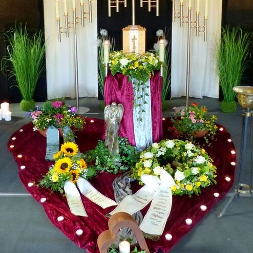 Dekorierter Altar mit Blumenarrangements, Kerzen und einer Statue in Herzform. Stoffe und Kerzen schaffen eine feierliche Atmosphäre.