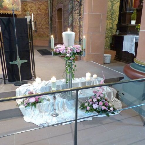 Blumenarrangement mit Kerzen und einer weißen Kerze auf einem silbernen Untergrund in einer Kirche.