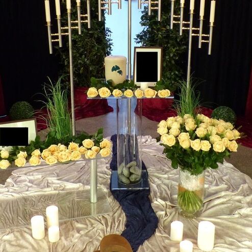 Dekorative Blumenarrangements mit weißen Rosen, Kerzen und Bildern auf einem festlich gedeckten Tisch.