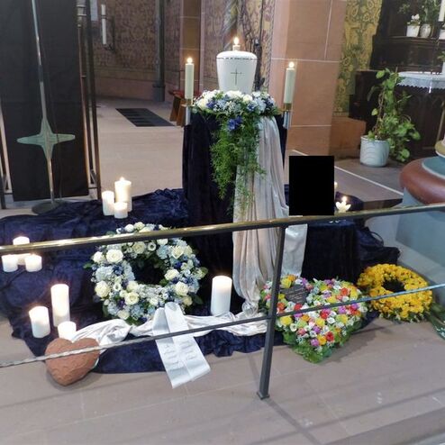 Gedenkaltar in einer Kirche mit Kerzen, Blumenkränzen und einem weißen Tuch auf einem Tisch.