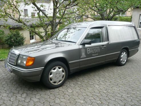 Fahrzeug mit geschlossener Ladefläche und Beschriftung „Bausen Boppard“ steht auf gepflasterter Fläche vor Bäumen.