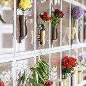 Blumengestecke in Vasen an einer transparenten Wand mit Grabinschriften.
